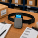 Gray AgozTech Almex Mobile Terminal Waist Belt Case for inventory teams staged on a warehouse workstation with barcode sheets, pick list, SKU carton, and black waist belt.