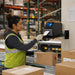 Warehouse worker pulling a shipping label from a SATO printer on an AgozTech wall mount shelf near conveyor boxes.