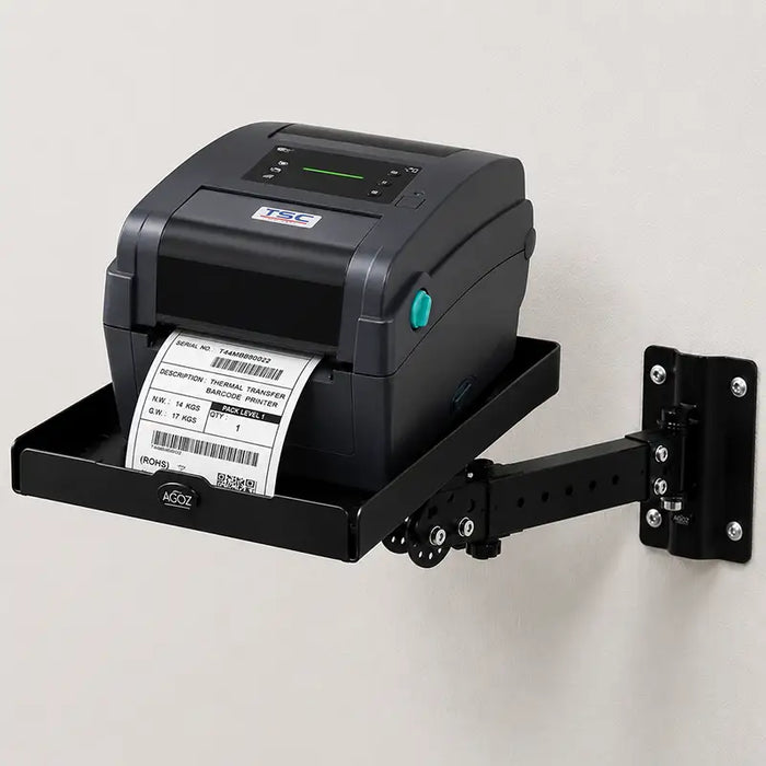 TSC desktop label printer on an AgozTech black wall mount printer shelf with adjustable arm, printing a barcode label against a light wall.