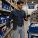 Warehouse worker holding a Datalogic handheld scanner in a picking area while wearing a smaller, empty black AGOZ case on his belt.