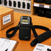 Black Cognex barcode reader sling holster staged on a warehouse workstation with barcode labels, pick list, and shipping supplies.