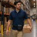 Warehouse worker wearing an Agoz Citizen mobile printer belt while carrying a package in a logistics center